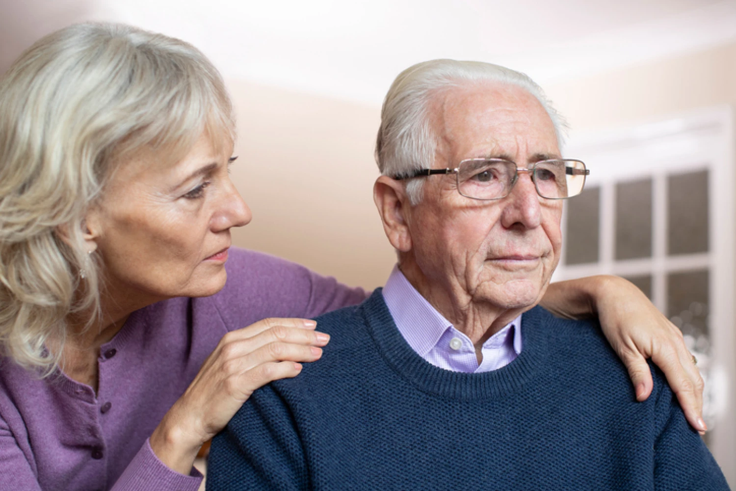 Elderly man with glasses looking concerned while being comforted by his partner, symbolising the emotional impact of dementia.