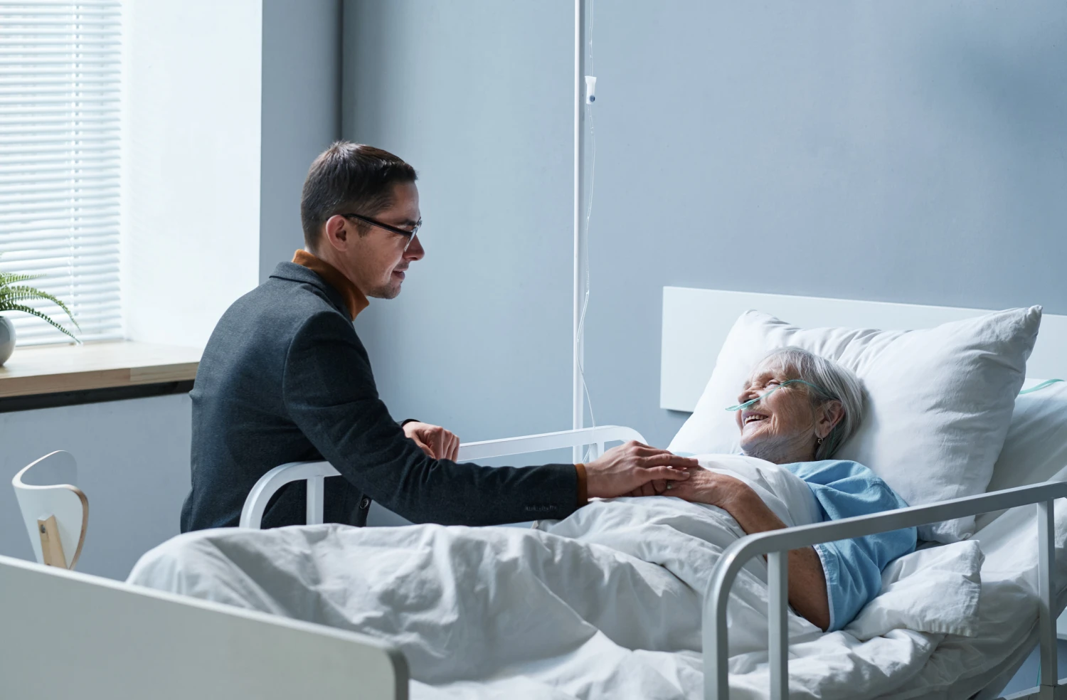 son visiting mother at palliative care, they are talking as she lays in bed