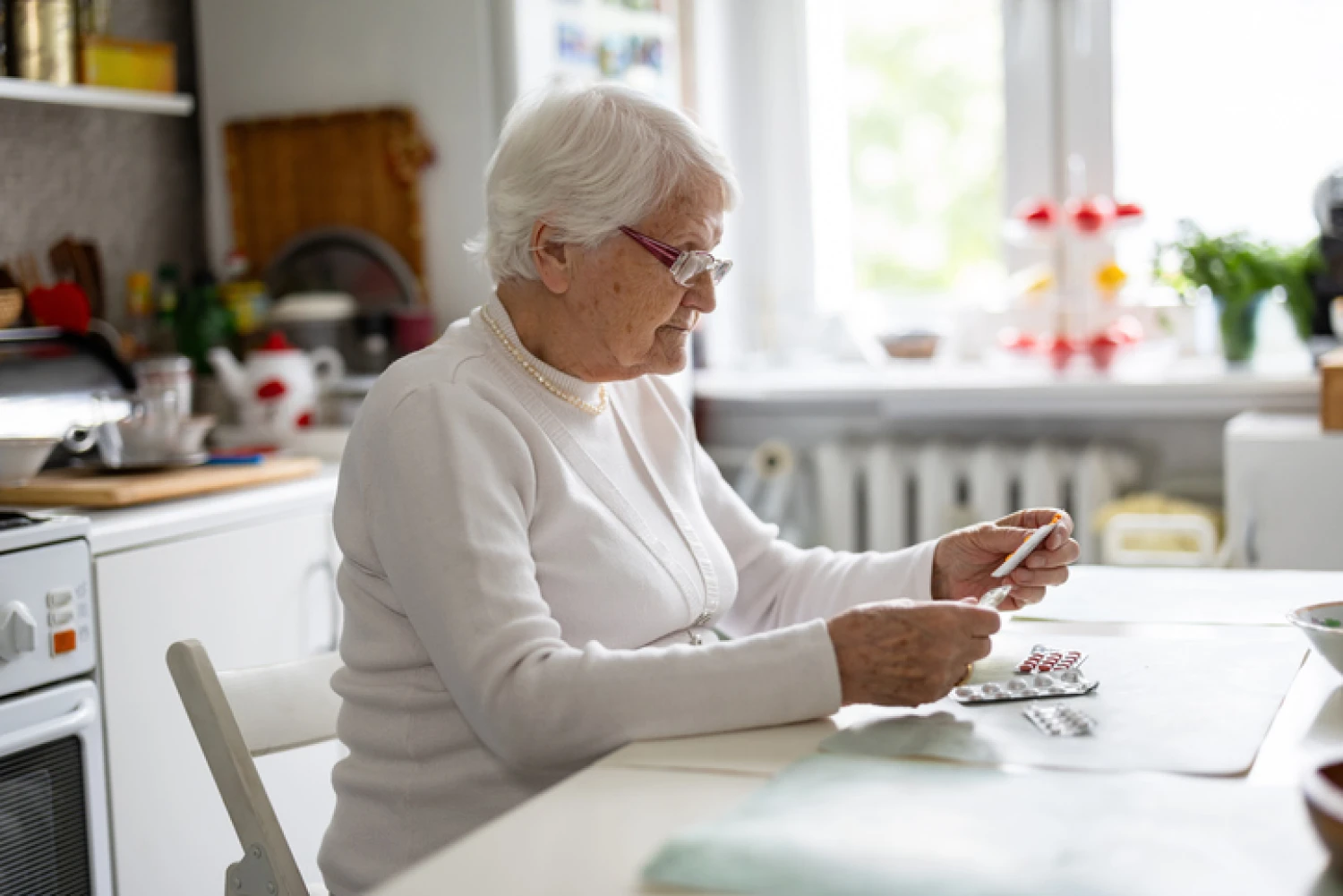An elderly woman sits at a kitchen table, with her medication, demonstrating daily medicine routine in dementia management.