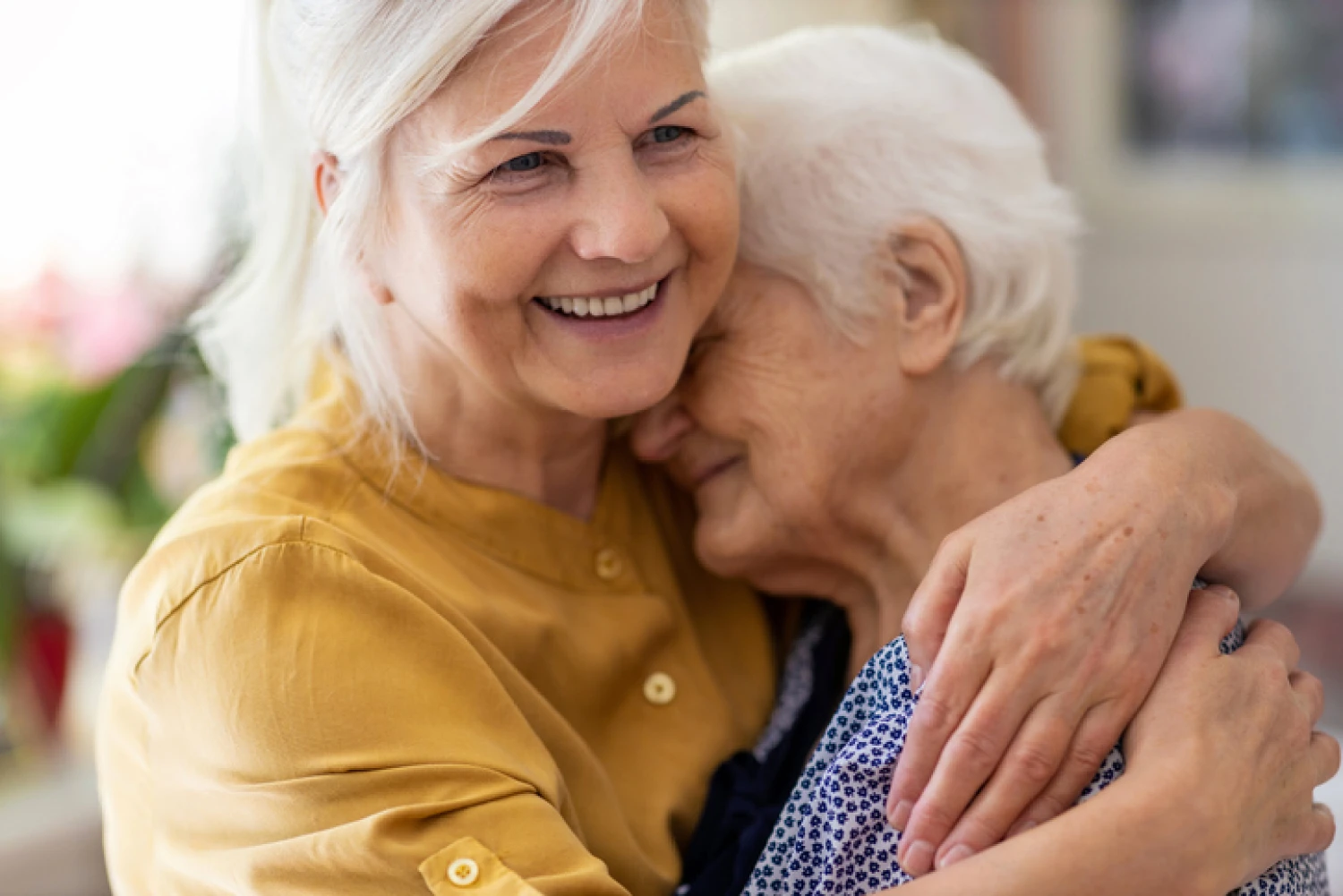 Smiling elderly woman hugging her elderly mother, illustrating the importance of emotional support in dementia care.