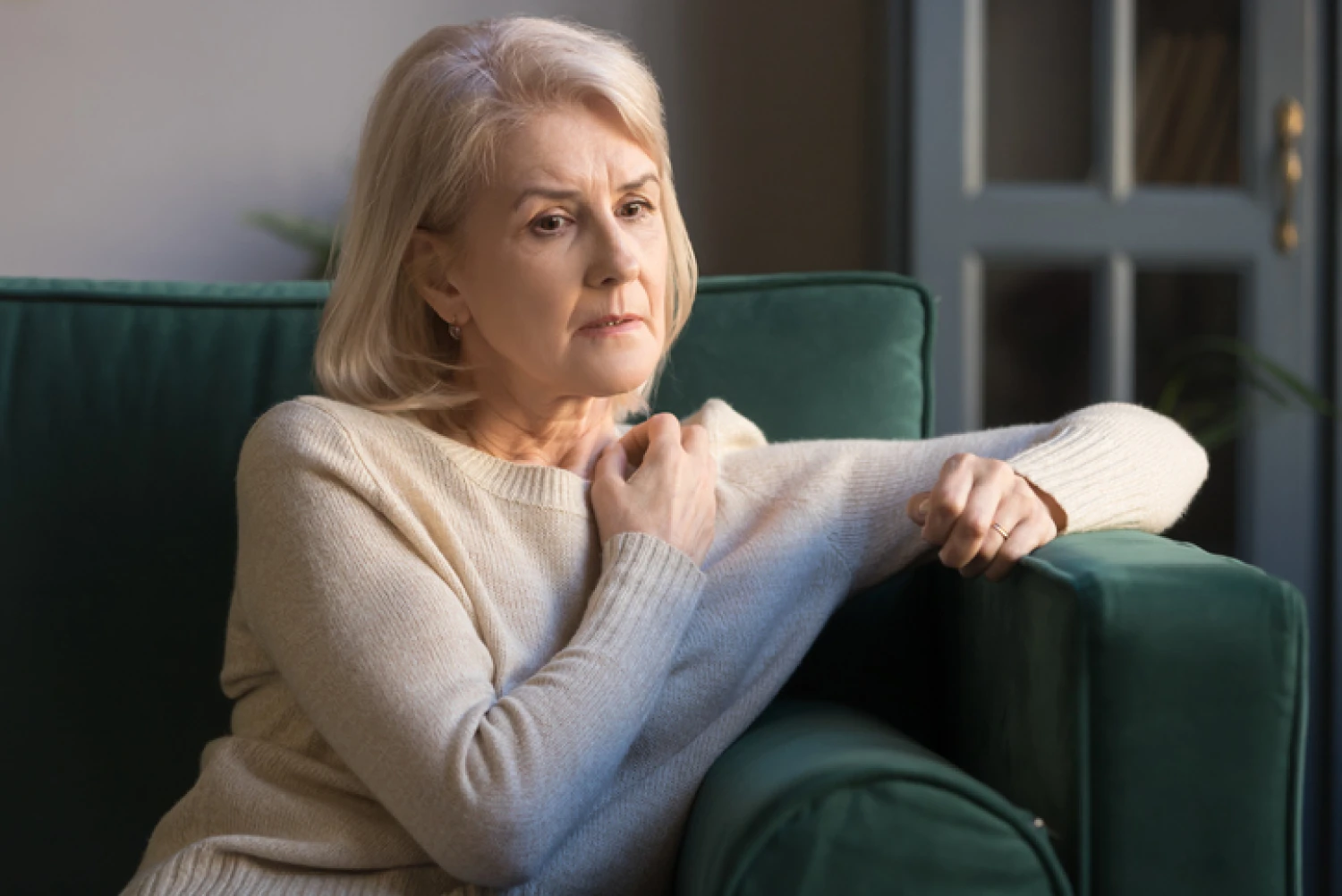 lderly woman with a worried expression sitting on a green sofa, depicting the anxiety and concern related to potential dementia symptoms.